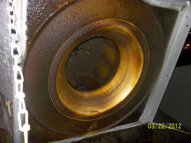 A rusty exhaust fan with a hole in it.